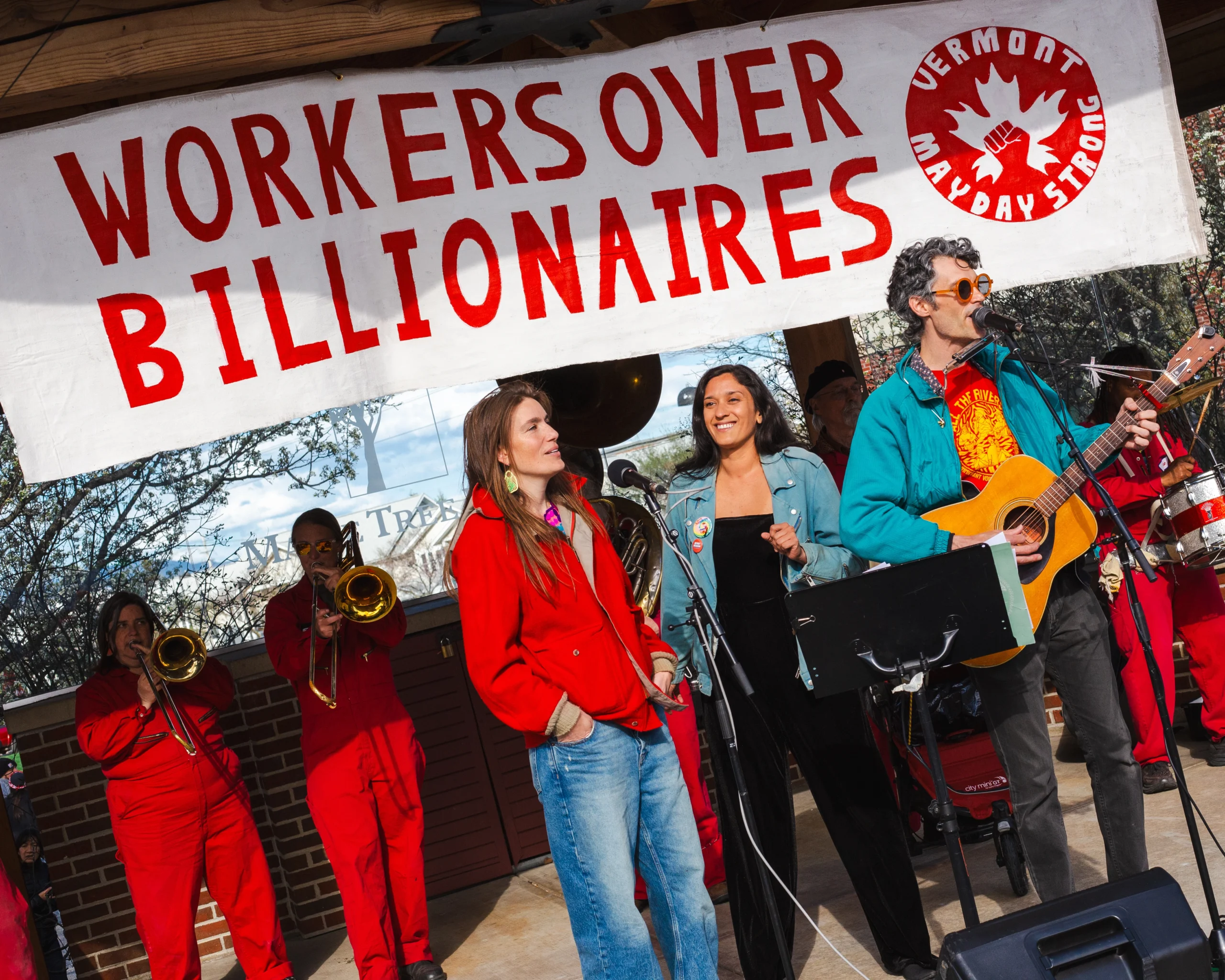 Amanda Janoo on stage in front of a "Workers over Billionaires" banner